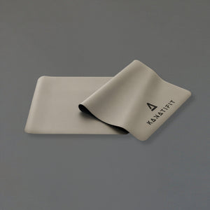 A light beige yoga mat with the brand name ''KANATIFIT' printed in black, shown partially rolled on a solid gray background.