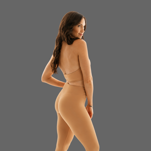 A woman modeling a nude-beige set from the back against a solid dark gray studio background.