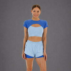 A woman modeling a matching athletic set consisting of a light blue and royal blue short-sleeve crop top and light blue running shorts, with the brand name 'KANATIFIT' visible on the front.
