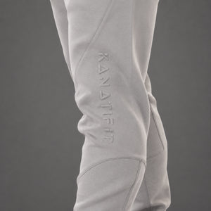 Close-up of light gray athletic pants worn on a model's leg, featuring an embossed vertical 'KANATIFIT' logo on the side, against a solid dark gray background.