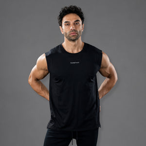 A muscular man wearing a black sleeveless athletic tank top with a small white 'KANATIFIT' logo on the chest, posed against a solid dark gray studio background.