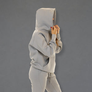 A person wearing a light gray hooded sweatshirt and matching jogger pants, shown from the side against a plain gray studio background.