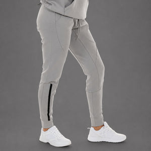 Light gray jogger pants with a black side stripe detail on the lower leg, shown on a model wearing white sneakers against a solid gray studio background.