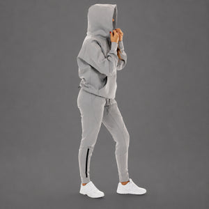 A model wearing a light gray hooded sweatshirt and matching jogger pants with a black side stripe, paired with white sneakers, shown against a solid gray studio background.