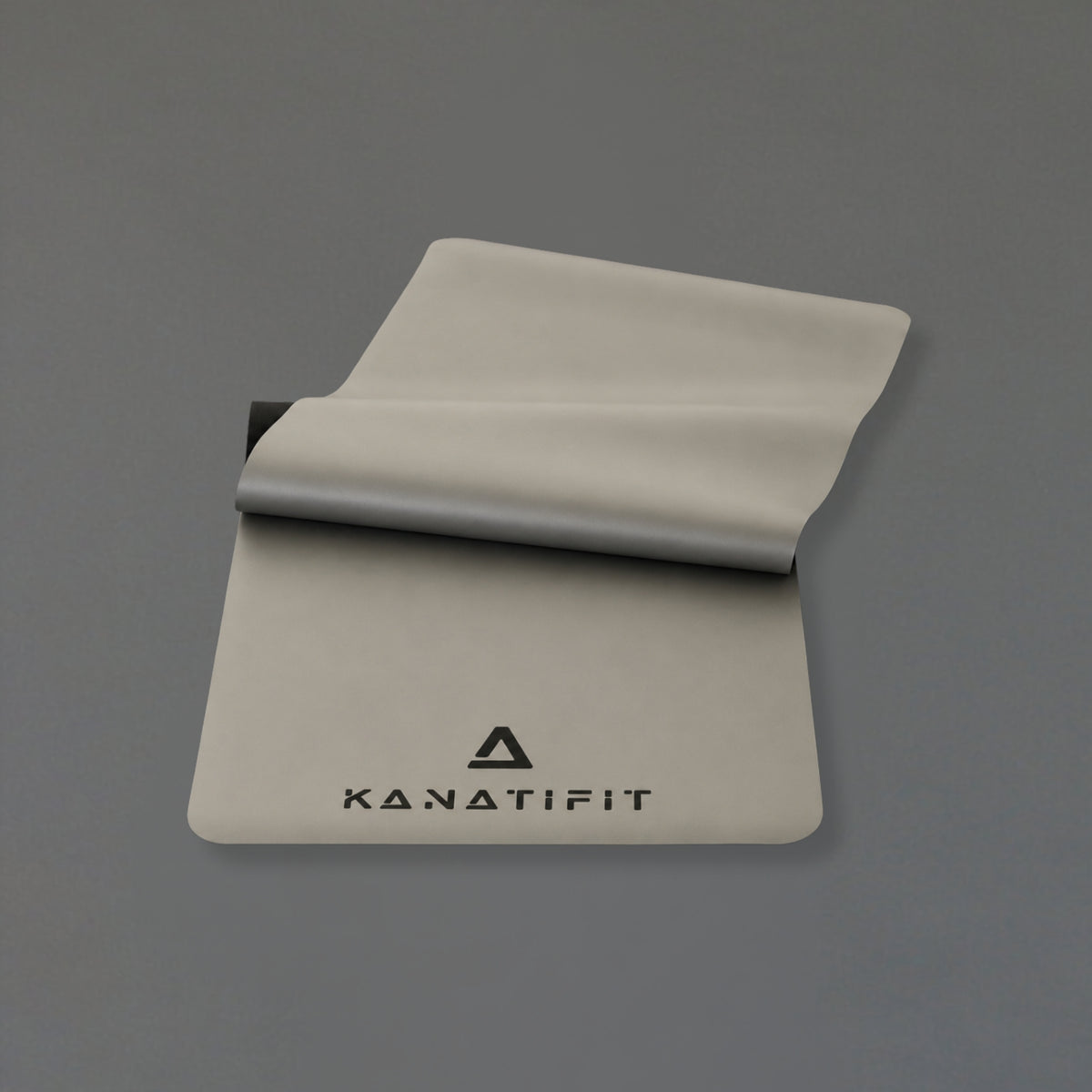 A light gray yoga mat with the KANATIFIT logo printed in black, shown partially unrolled on a solid gray background.