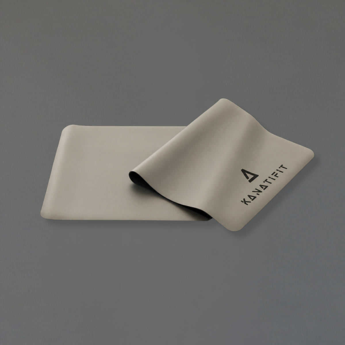 A light beige yoga mat with the brand name ''KANATIFIT' printed in black, shown partially rolled on a solid gray background.