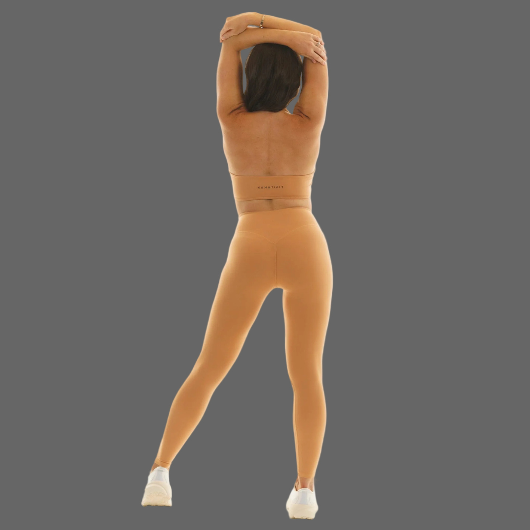 A person shown from the back wearing a matching beige/tan two-piece outfit with a fitted crop top and high-waisted leggings, standing against a plain gray background.