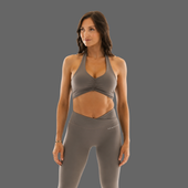 A woman modeling a matching gray athletic set consisting of a ruched halter sports bra and high-waisted leggings, shown against a solid gray studio background.