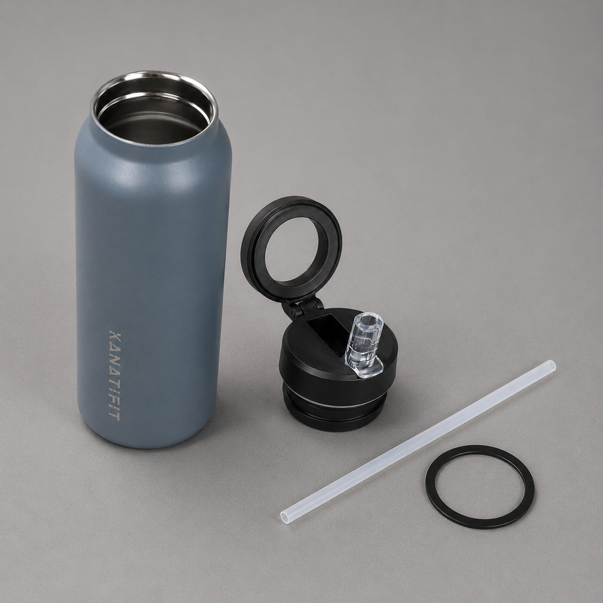 A matte slate insulated water bottle with a stainless steel interior, shown next to its open black lid, a clear straw, and a black ring on a neutral gray background. The brand name 'KANATIFIT' is printed vertically on the bottle.
