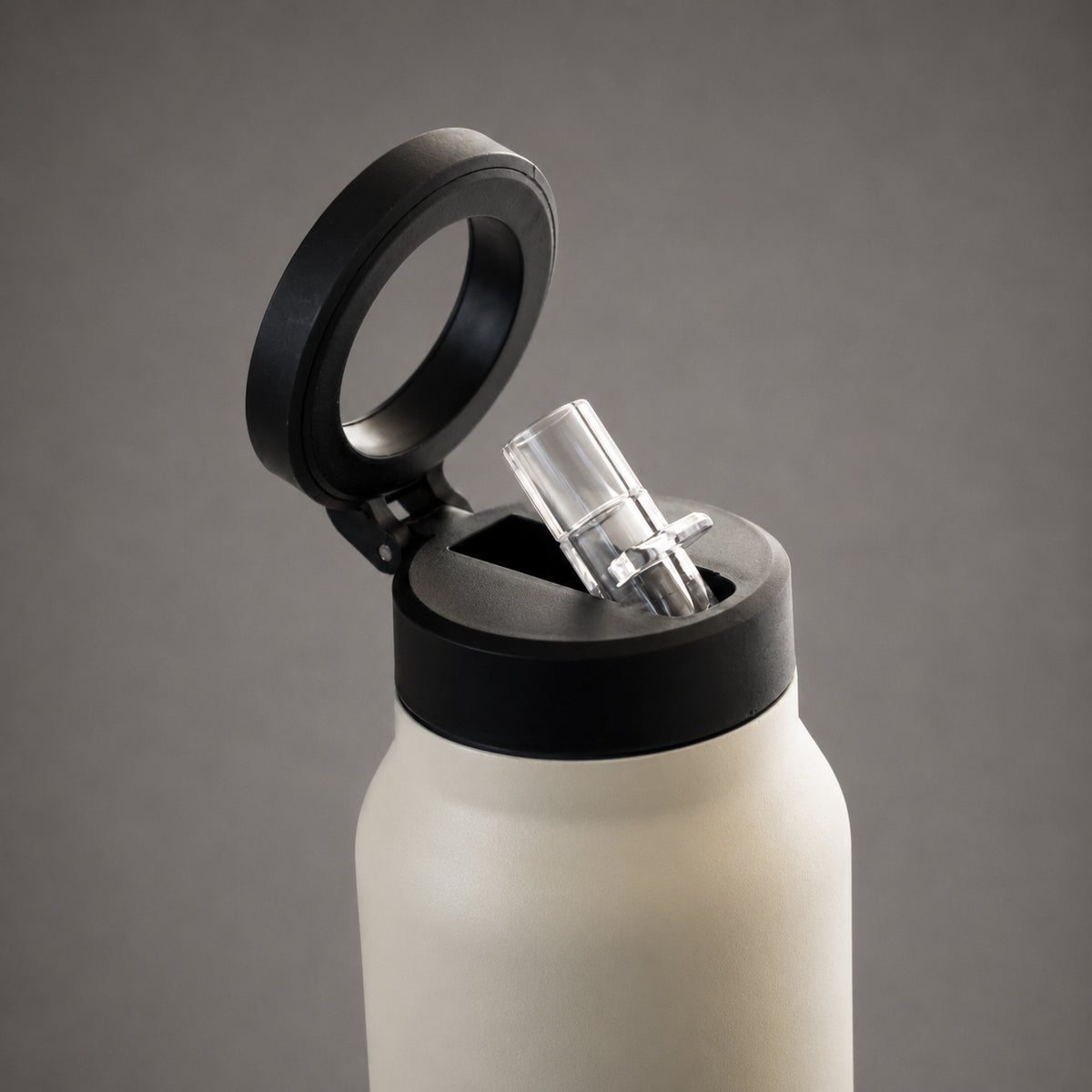 A close-up of a matte white insulated bottle with a black lid and an open flip-top style clear straw insert, shown against a smooth gray studio background.
