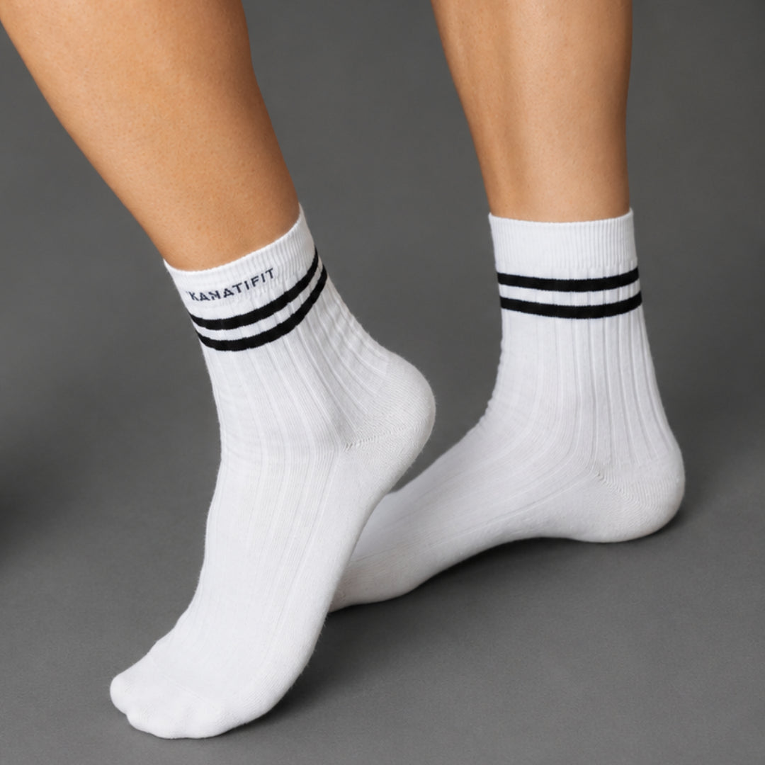 White ankle socks with black stripes and the brand name 'KANATIFIT' printed on the cuff, shown on a model's feet against a gray background.