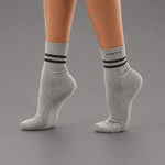 A pair of light gray heather ankle socks with two black stripes and the brand name 'KANATIFIT' printed on the cuff, shown on a model's feet against a solid gray background.