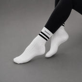 White ankle socks with black stripes and the brand name 'KANATIFIT' printed on the cuff, worn with black leggings against a neutral gray background.