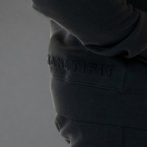 Close-up of a dark charcoal gray hoodie with the brand name 'KANATIFIT' embossed on the chest, shown on a model against a neutral gray background.