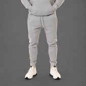 A person wearing a light gray matching sweatshirt and jogger pants set, shown from the chest down against a dark gray studio background. The person is wearing white sneakers.