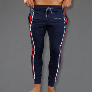 A person wearing navy track pants with red and white side stripes, shown from the waist down against a plain gray background. The pants have a drawstring waist and a small white 'KANSASFIT' logo on the right hip.