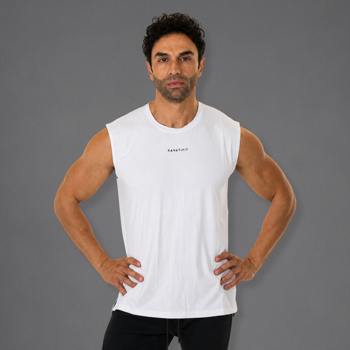 A man modeling a white sleeveless athletic tank top with a small black 'KANATIFIT' logo on the chest, set against a solid gray studio background.