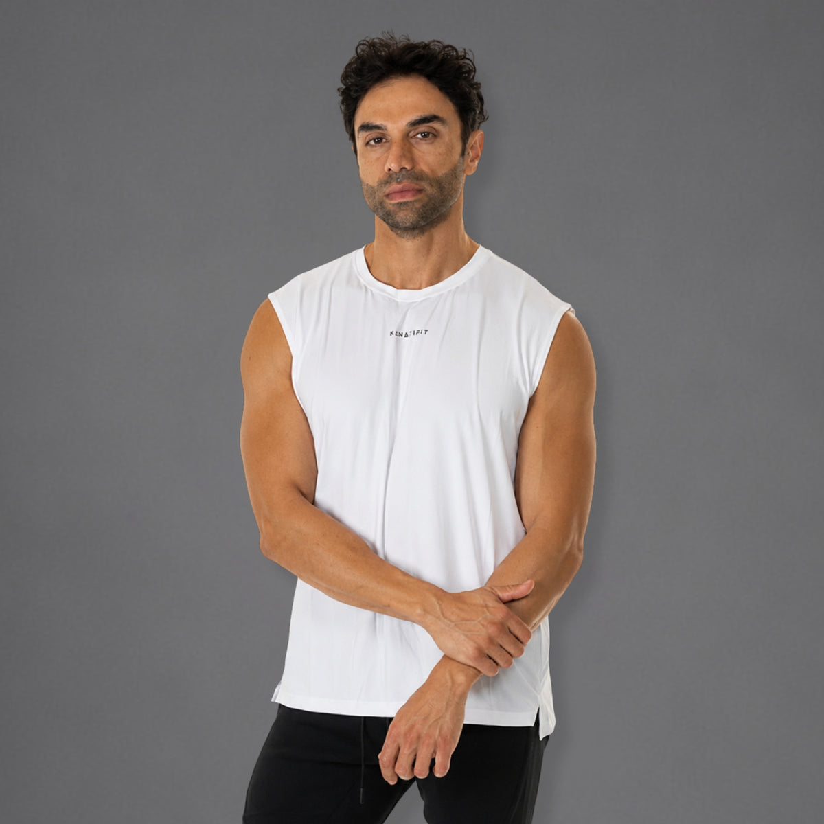 A man wearing a white sleeveless athletic tank top with a small black logo on the chest, posed against a solid gray studio background.