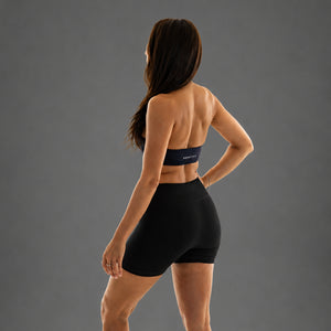 A woman shown from the back wearing a matching black sports bra and high-waisted athletic shorts against a solid gray studio background.