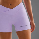 A close-up of a model wearing a grape coloured ribbed athletic shorts with a crossover waistband and the brand name KANATIFIT printed in black near the hem.