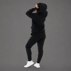 A model wearing a matching black hoodie and jogger sweatpants set, shown from the back and side against a solid gray studio background.