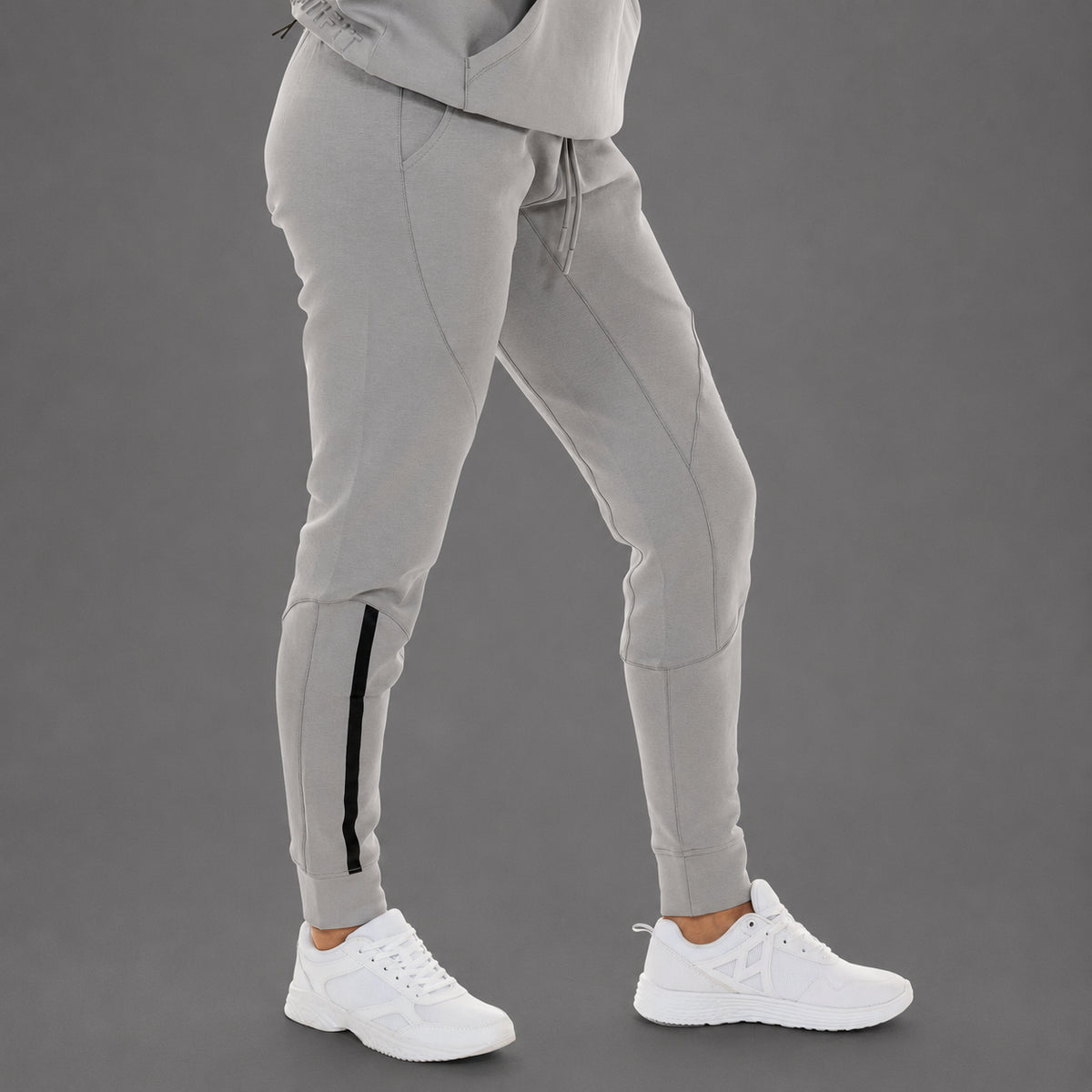 Light gray jogger pants with a black side stripe detail on the lower leg, shown on a model wearing white sneakers against a solid gray studio background.