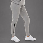 Light gray jogger pants with a black side stripe detail on the lower leg, shown on a model wearing white sneakers against a solid gray studio background.